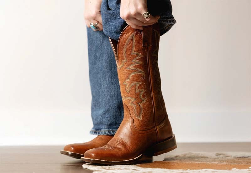 A woman putting the Madison 11” Western Wide Square Toe boot in brown.